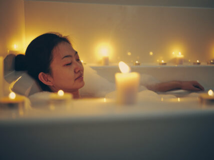 A young Japanese woman relaxing in a bathtub, surrounded by candles.